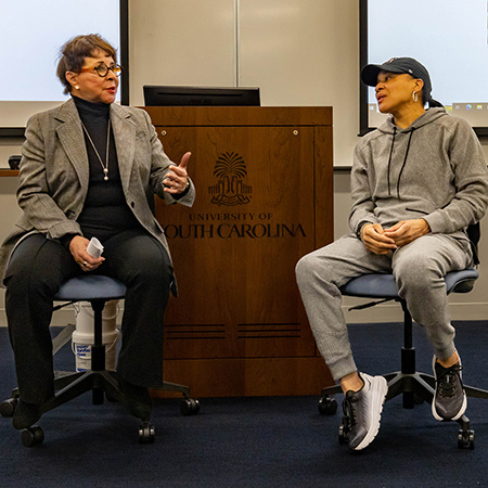 Sheila Johnson and Dawn Staley talk with one another in front of a class.