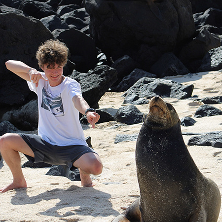 A student in the Galapagos Islands points at a sea lion on the beach.