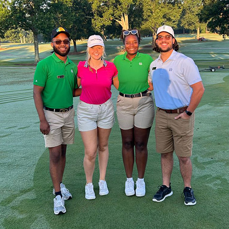 Four students pose on a golf course