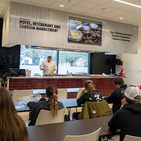 A chef instructor prepares food in the Marriott Culinary Lab while students watch.