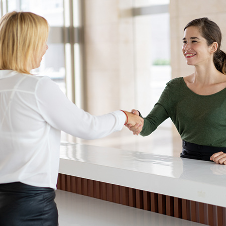 Two people shake hands at a reception desk.