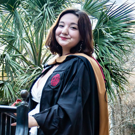 MIHTM graduate Ashlyn Ooi poses for a photo in her cap and gown in front of McCutchen House.
