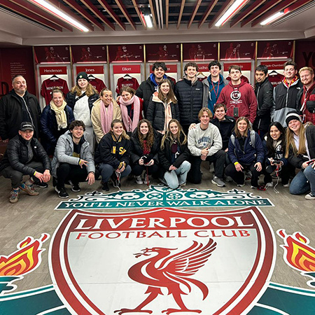 A group of HRSM students and faculty/staff pose for a picture inside the Liverpool Football Club locker room while visiting on a study abroad strip.