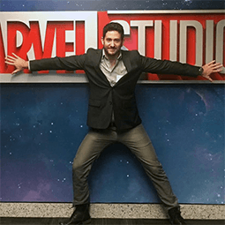 Brandon Davis stands with arms spread across a Marvel Studios sign