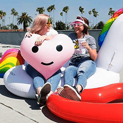 Rachel Gannon and a friend sit on their colorful fun pool floats at the edge of a pool