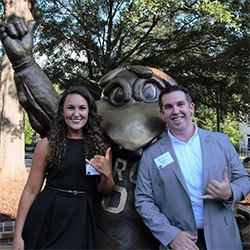 Tara Parker and Blake Edmunds stand with the bronze statue of Cocky giving the "spurs up" hand signal