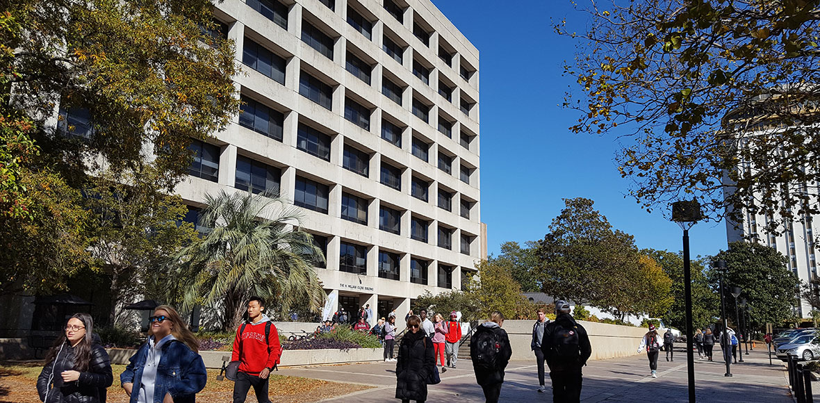 Students walk in front of the Close-Hipp building on a clear fall day. The Close-Hipp building is located in the historic center of South Carolina's campus.