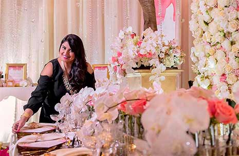 Nirjary Desai sets formal place settings on a beautifully dressed table in a room full of pink and cream roses, peonies and other flowers