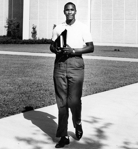 Black and white photo of Ernest Boger in 1961 walking with his books, on the campus of the University of South Florida