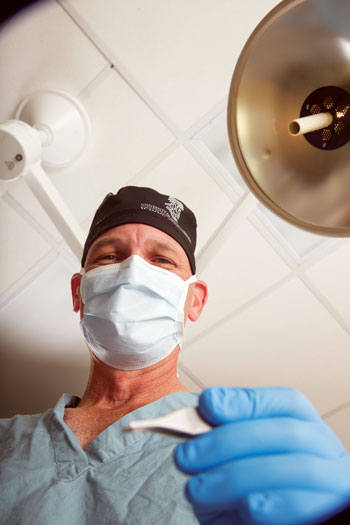 Dr. Clair holding a scalpel and wearing gloves and a mask