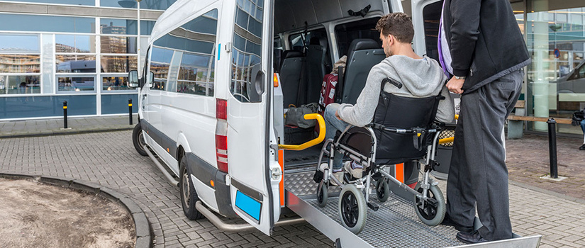 A man in a wheelchair is assisted on a van ramp