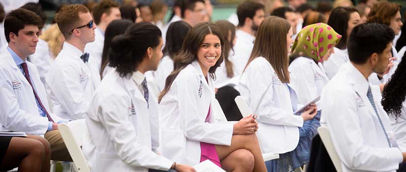 Female med student sits in row with other students at outdoor ceremony