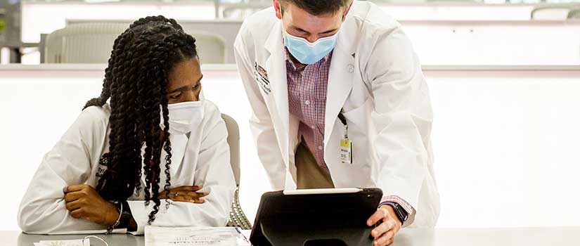 Male and female med students look at an ipad in a well-lit classroom.