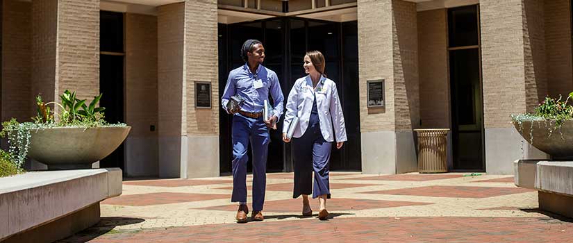 Black male and white female med students walking in front of hospital.