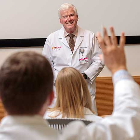 Medical Student raises his hand while mature professor smiles.