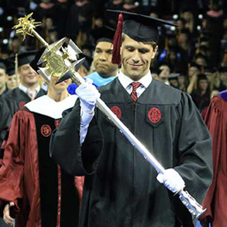 Student in cap and gown carries the mace in academic procession