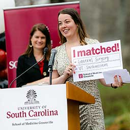 Med student holds an "I Matched" sign on stage