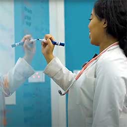 Female medical student writes on a reflective white board.