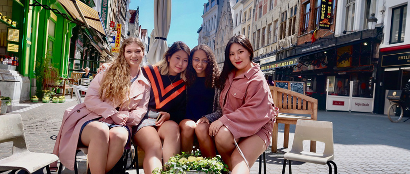 Four female students sitting outside on a village street in Belgium, France