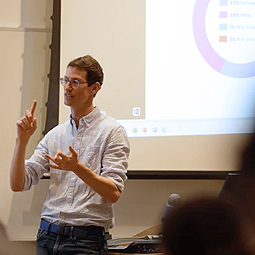 Joel Wootan teaching class, PowerPoint slide with graphs showing on screen behind him.