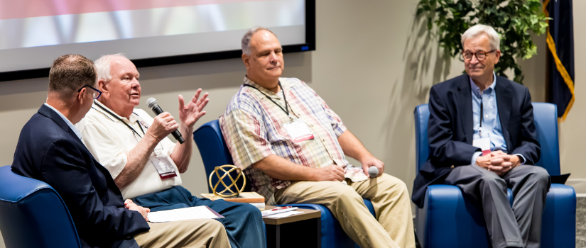 Panelists sitting in chairs on stage at a conference