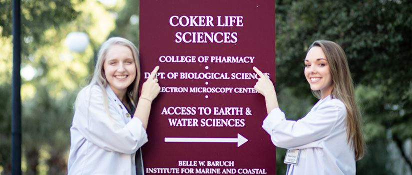 Two students pointing to Coker Life Sciences Building sign