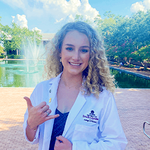 Student in white coat doing 'spurs up' hand gesture