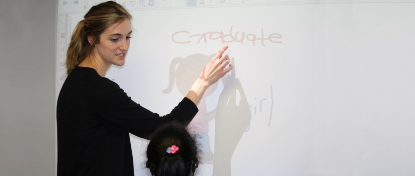 Student demonstrating something on a white board to a child