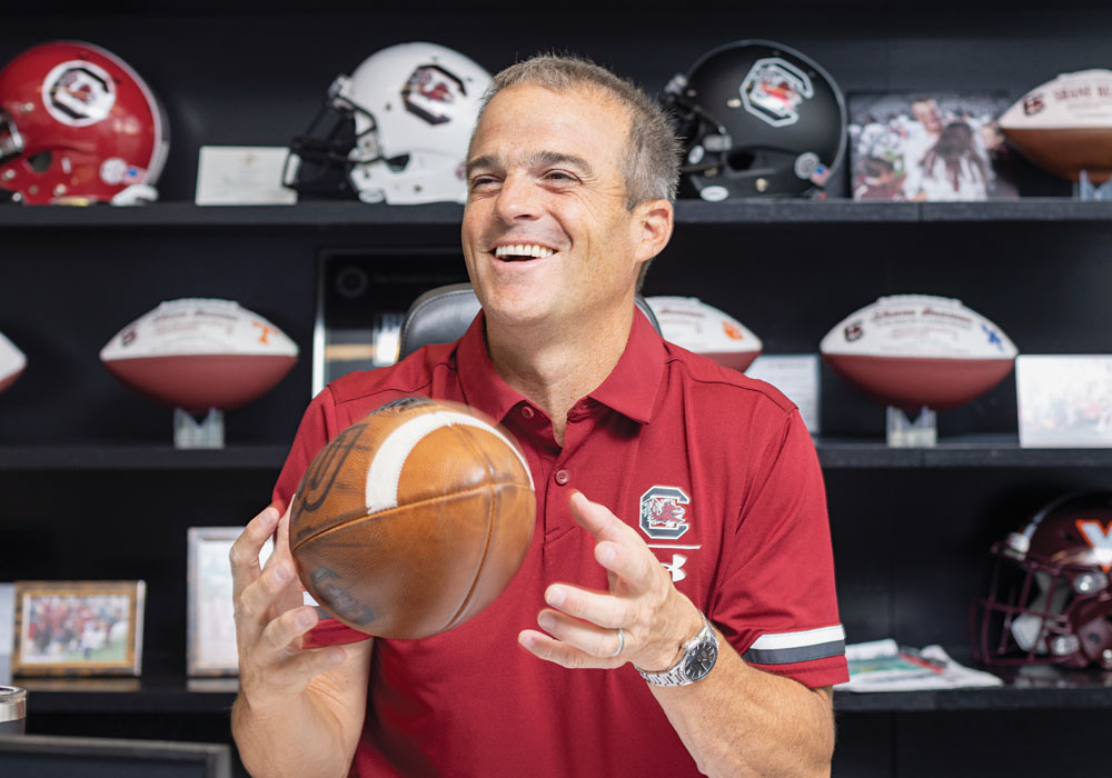 Shane Beamer laughs while holding a football in his office.