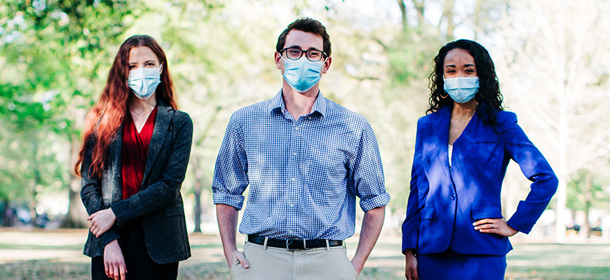 female student wearing mask in black skirt and garnet blouse, male student wearing mask in blue check shirt, female student wearing mask in blue suit