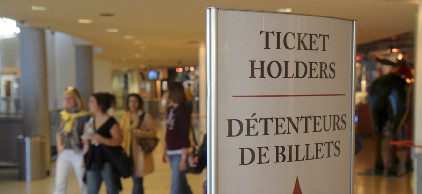 People walking in the lobby of a building focusing on a sign that says ticket holders with an arrow