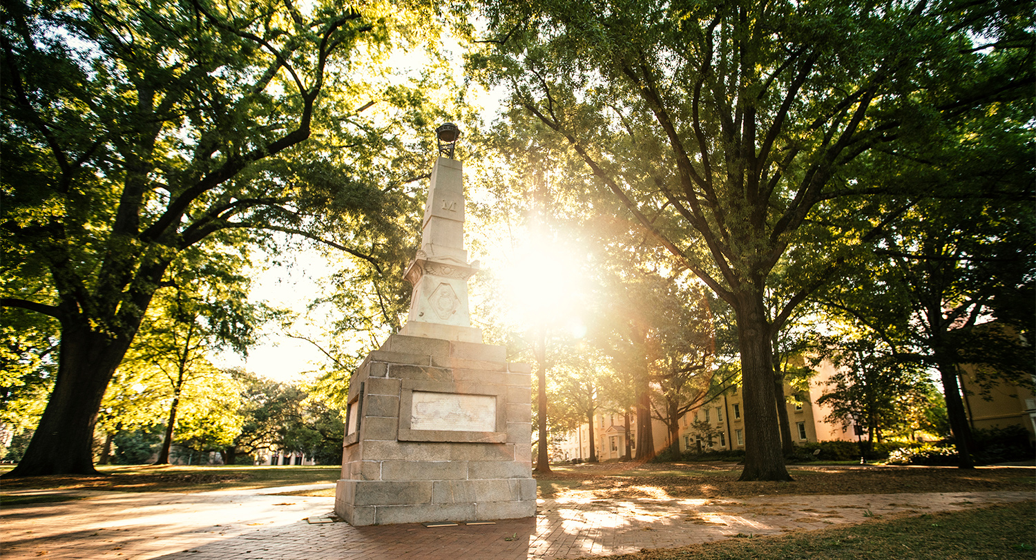 The sun shining through the trees behind the Maxcy Monument on the Historic Horseshoe. 