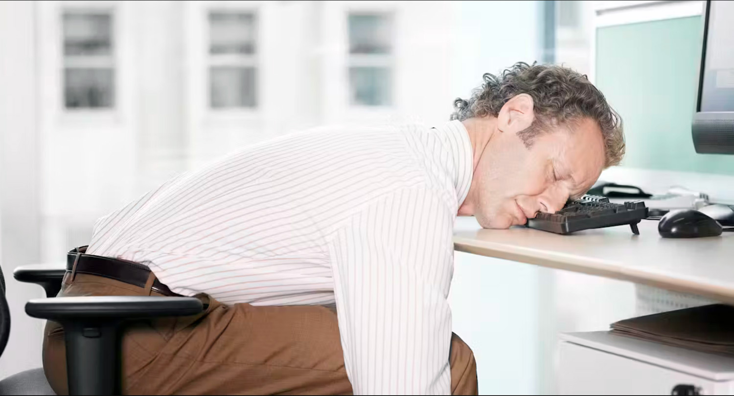 Man sitting in a desk chair resting his head on a keyboard