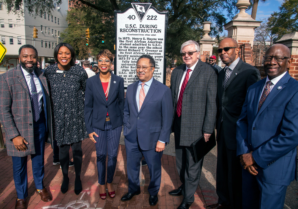 a group of people stand in front of a historical marker commemorating the enrollment of the first Black student at USC during reconstruction