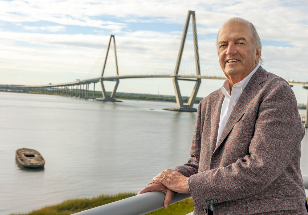 man leans on a railing with a river and cable-stayed bridge in the background
