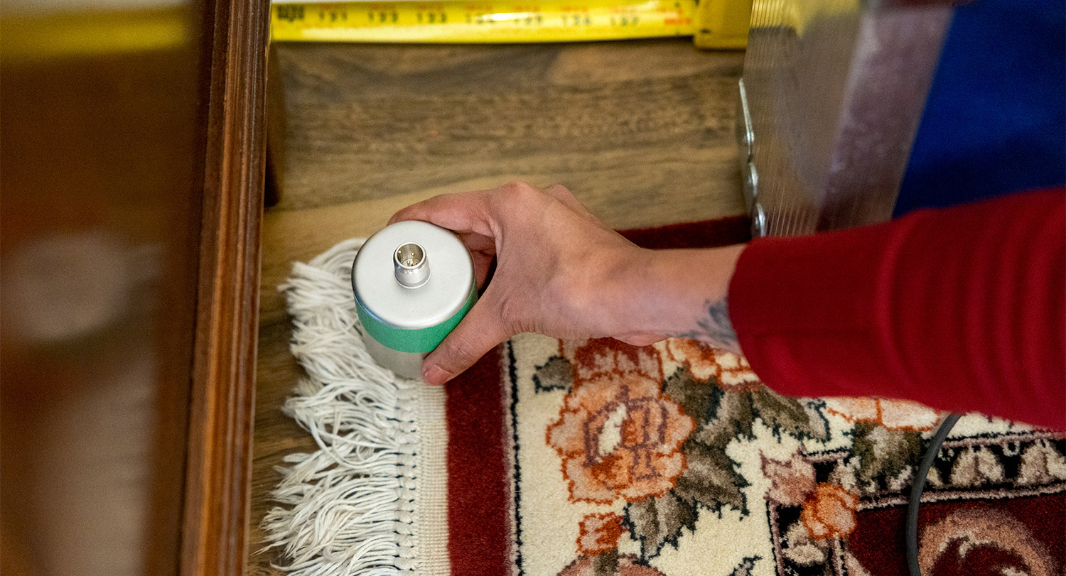A hand places a small sensor on a rug on a floor