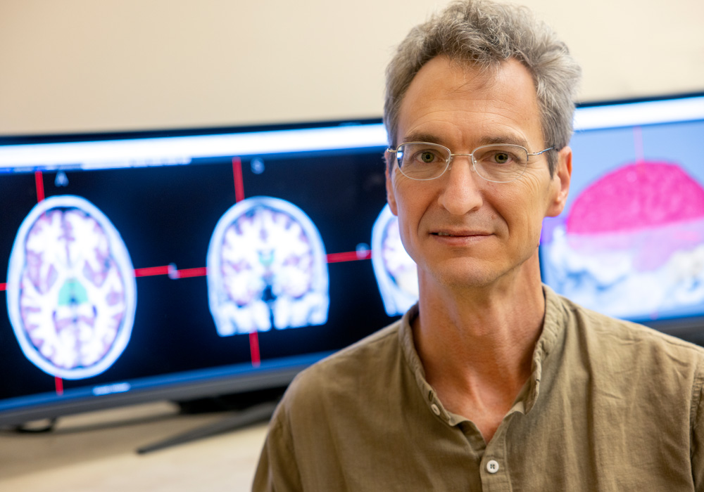 man sits in front of computer screens with brain images on display