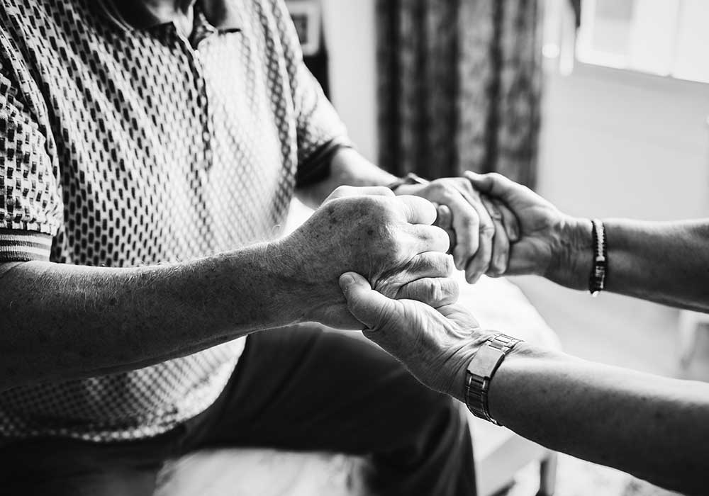 Female social worker holds hands of elderly male.