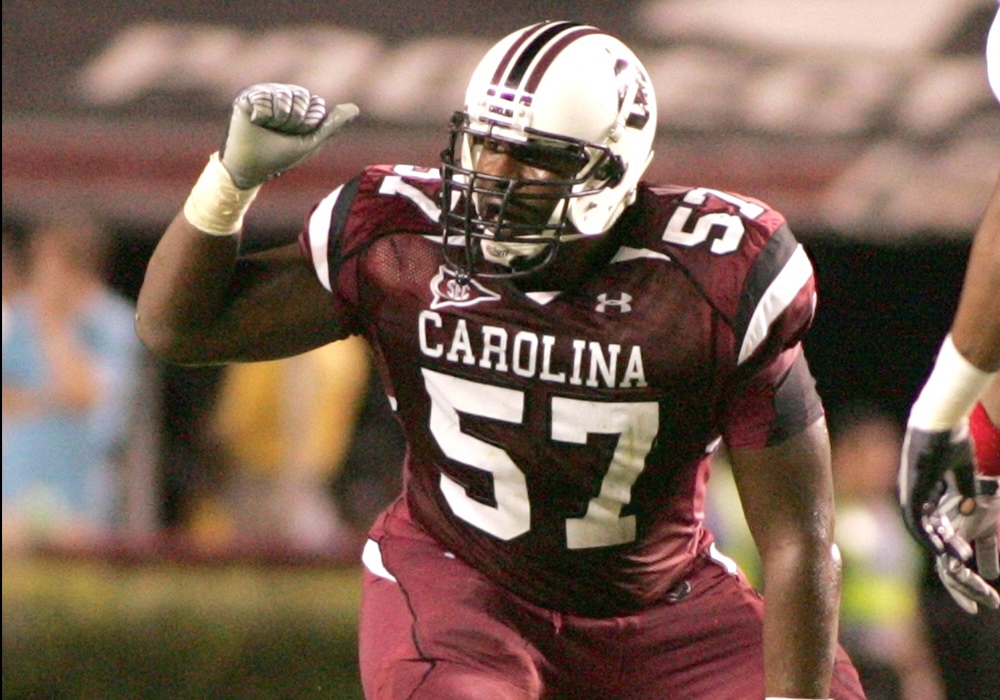 man in garnet football jersey crouches over football and points