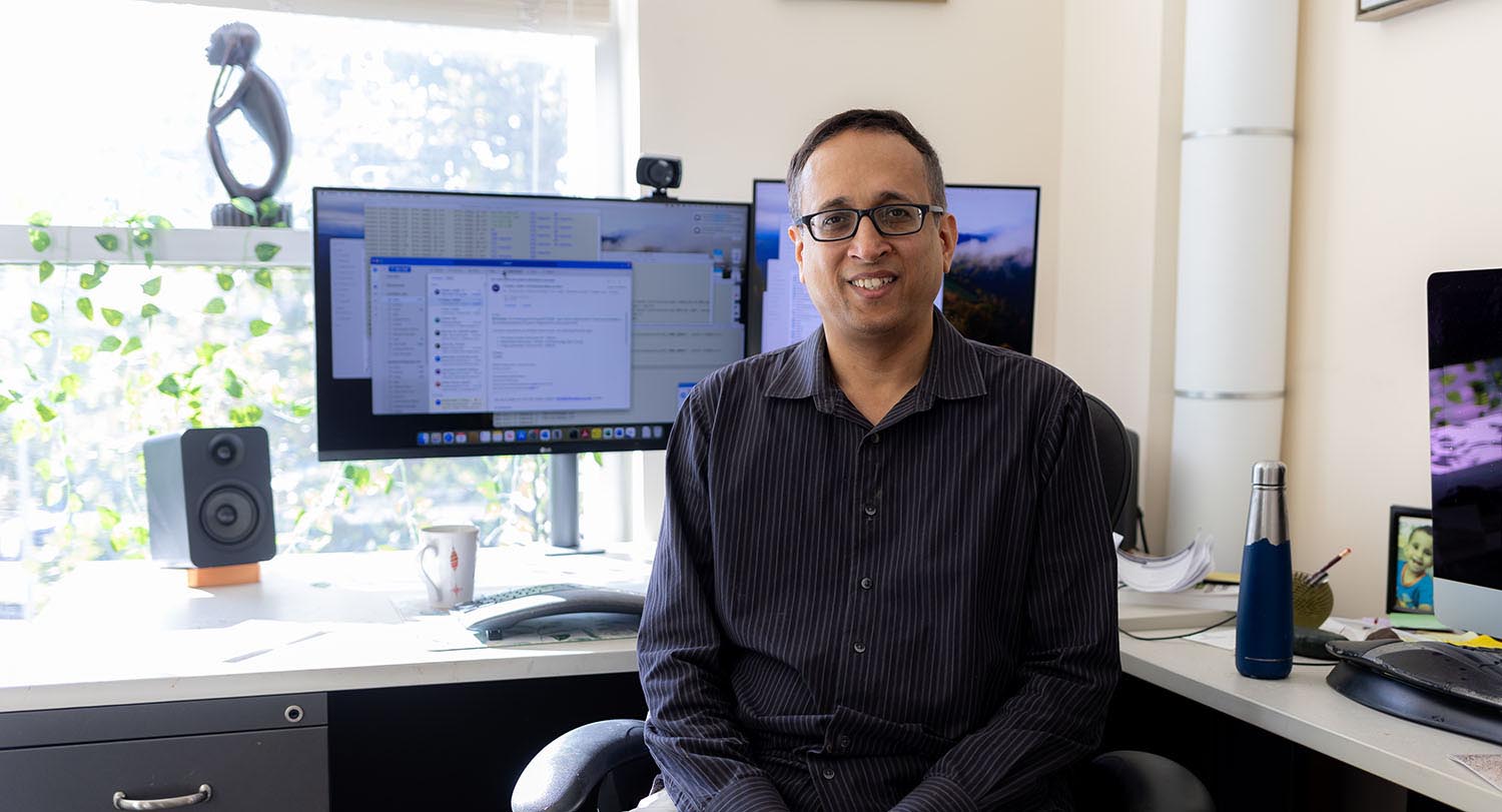 man sits at a desk with a computer and a window in the background