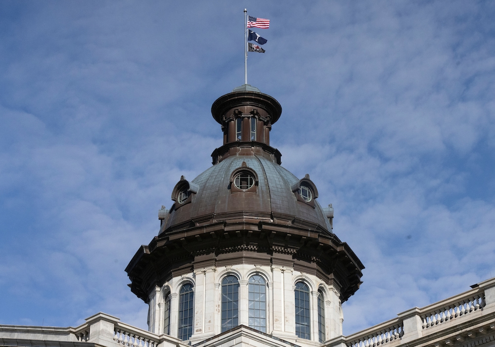 american flag, palmetto flag and USC flag flying above dome on statehouse