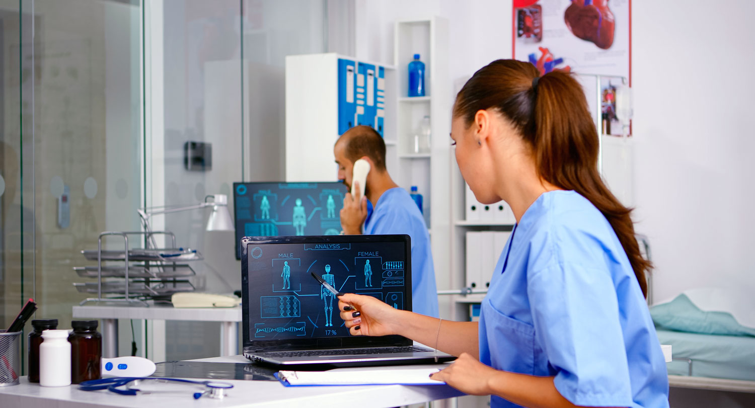 a health care worker looks at a computer screen with equipment in the background