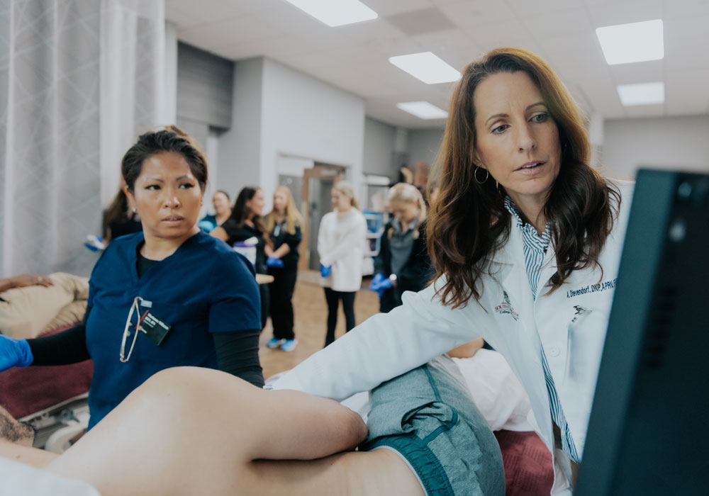 A nurse practitioner student watches nursing associate professor Amy Dievendorf demonstrate an ultrasound monitor.