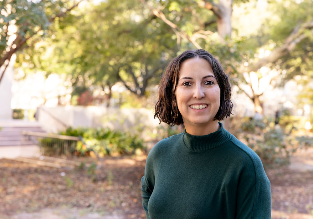 Woman stands outside with greenery in the background