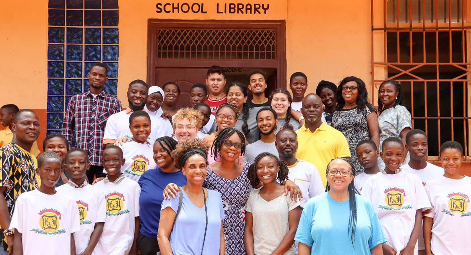 MInuette Floyd poses with students and teachers in front of a school library in Ghana.