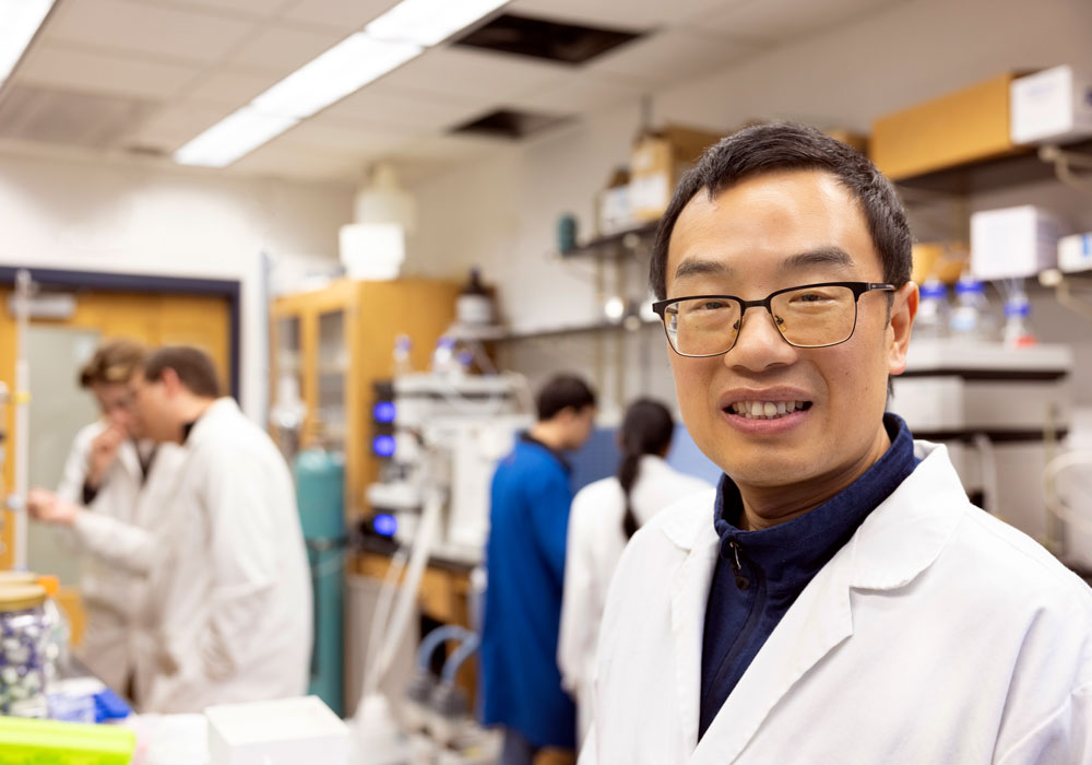 Man stands in a lab setting with equipment and people in the background