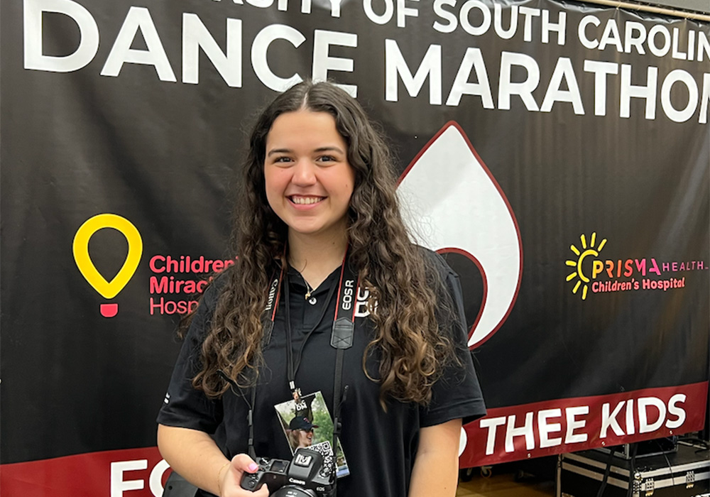 a woman stands in front of a sign that says Dance Marathon