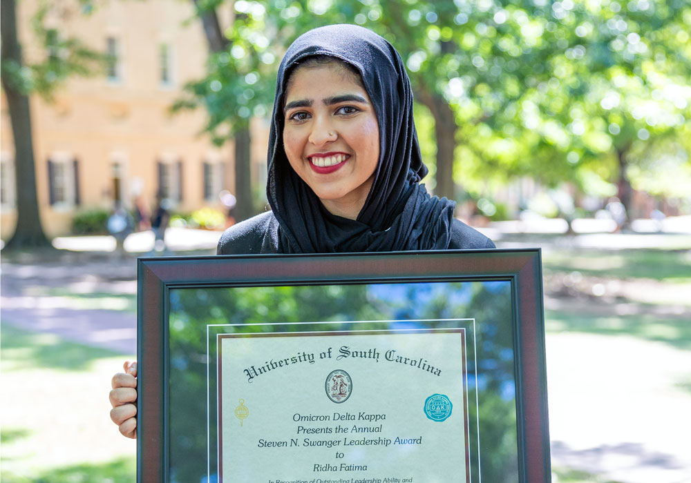 woman stands outside holding a framed award