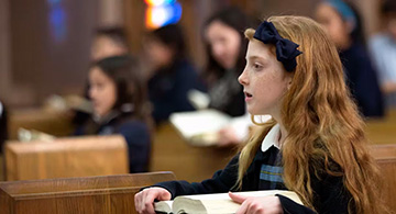 A red-headed girl in Catholic school uniform pays attention in class.