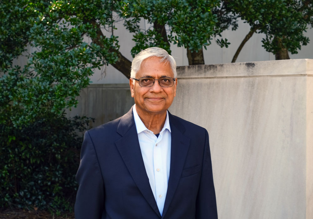 man stands in front of a building with greenery in the background